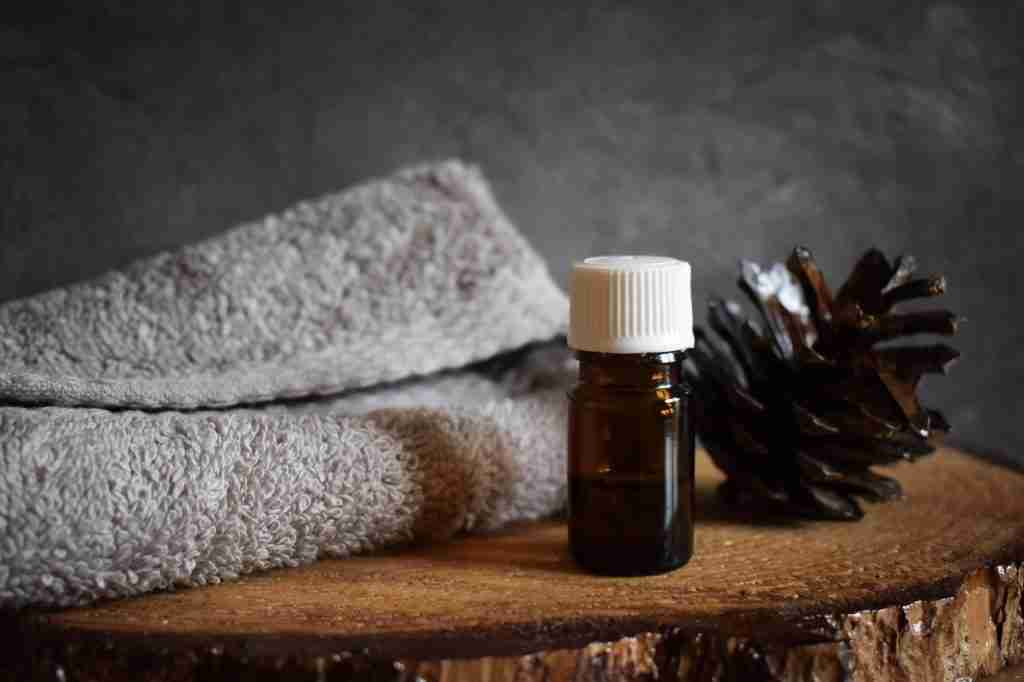 Aromatherapy essential oil bottle with pine cone, paired with towels for relaxation or spa treatments.
